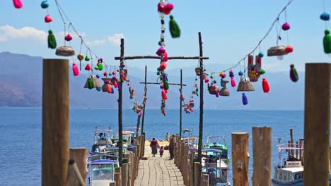 Long,-colourful-decorative-pier-with-old-lady-and-small-child-walking-in-Lake-Atitlan,-Guatemala