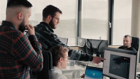 Group-of-three-young-men-discussing-a-stock-chart-in-front-of-a-computer-at-a-office-space-of-an-start-up-company