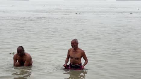 Front-view-of-men-talking-the-holy-dip-and-praying-in-foggy-winter-morning-during-Sankranti-with-seascape-at-background-in-Babughat,-Kolkata