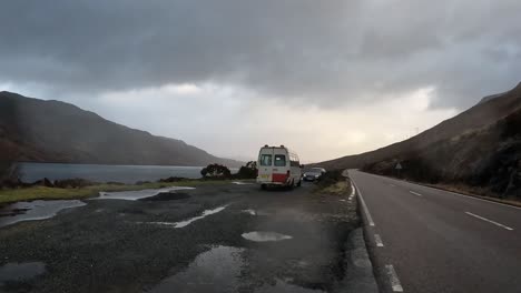 Día-Sombrío-En-La-Isla-De-Skye-Con-Vehículos-Estacionados-Al-Borde-De-La-Carretera,-Charcos-Reflectantes-Y-Montañas-Brumosas