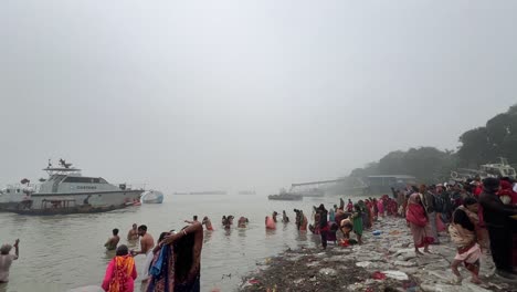 Wide-shot-of-men-and-woman-bathing-and-praying-in-foggy-winter-morning-during-Sankranti-with-jetty-in-the-background
