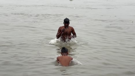 Two-boys-bathing-and-taking-holy-ganga-water-in-bottle-during-Sankranti-Hindu-festival-in-Babughat,-Kolkata-during-evening