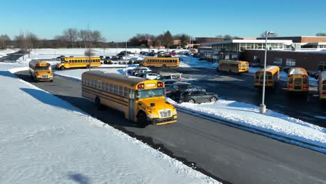 Buses-leaving-American-school-in-line-on-sunny-winter-day-with-snow