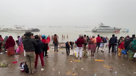 Wide-angle-static-shot-of-People-bathing-and-praying-during-Sankranti-near-a-jetty-in-Babughat,-Kolkata-during-foggy-evening