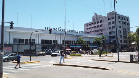 Panoramic-Location-of-Train-Station-at-Latin-City-under-Sunny-Midday-People-Walk-in-Hot-Asphalt,-Federico-Lacroze-Railway,-General-Urquiza