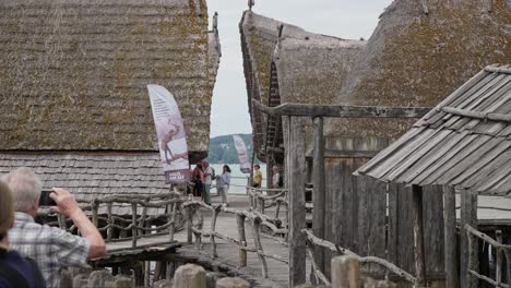 Thatched-roofs-of-traditional-Ice-Age-dwellings-at-a-museum-exhibit,-people-exploring