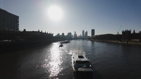 Uber-River-Boat-glides-on-the-Thames-at-Westminster,-London,-bathed-in-the-glow-of-a-low-angle-sun