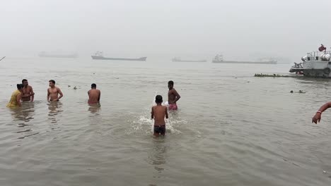Profile-view-of-people-bathing-and-praying-in-foggy-winter-morning-during-Sankranti-festival-with-jetty-in-the-background