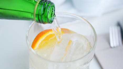 Pouring-soda-into-glass-with-ice-and-slice-of-orange,-close-up