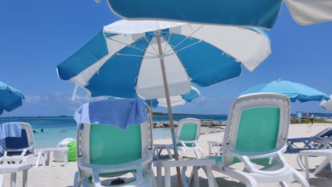 Genießen-Sie-Den-Karibischen-Charme:-Leere-Stühle-Mit-Sonnenschirmen-Zieren-Den-Sandstrand,-Umrahmt-Von-Leuchtend-Blauem-Wasser-Und-Himmel,-Der-Gelassenheit-Und-Tropische-Glückseligkeit-Hervorruft