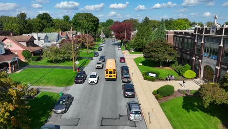 Yellow-school-bus-driving-past-American-high-school-with-students-leaving-at-dismissal