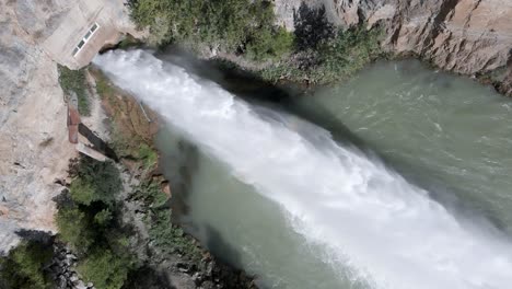 Jet-of-water-emerges-from-Arenoso-Reservoir-spillway,-El-Chorro,-Spain,-aerial-top-down