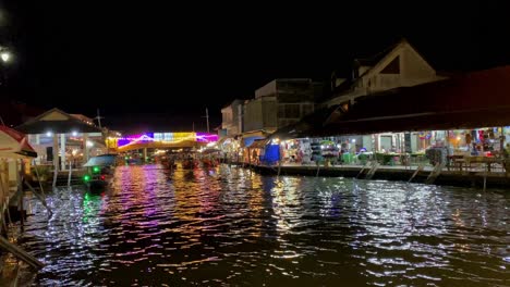Nachtansicht-Eines-Lebhaften-Schwimmenden-Marktes-Mit-Beleuchteten-Geschäften-Und-Spiegelungen-Auf-Dem-Wasser