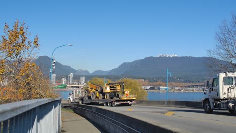 Construction-equipment-on-trailer-with-Vancouver-skyline,-clear-day