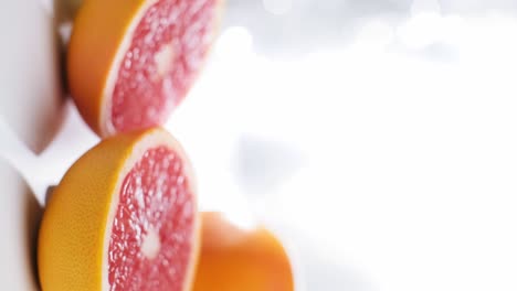 Vertikales-Video-Von-Grapefruithälften-Auf-Einer-Weiß-Reflektierten-Oberfläche,-Dolly-In-Zeitlupe