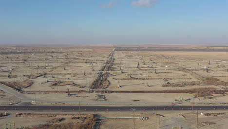 Drone-flying-backwards-over-wells-with-pump-jacks-on-oil-field,-California-USA