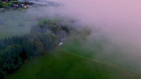 Aerial-drone-top-down-shot-over-green-agricultural-fields-through-white-clouds-with-the-view-of-village-houses-in-the-background-on-a-cloudy-day