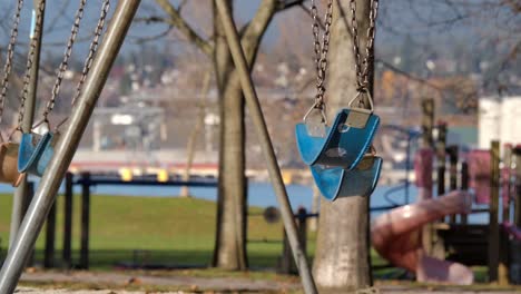 Empty-blue-swings-in-park-with-blurry-background,-daylight,-slow-motion