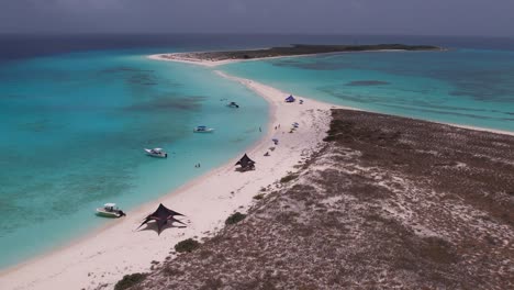Aerial-view-of-Cayo-de-Agua-featuring-serene-beach,-clear-turquoise-waters,-boats,-tranquil-mood,-overcast-sky