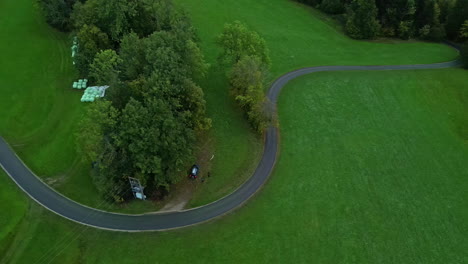 Aerial-drone-top-down-shot-over-a-winding-road-surrounded-by-green-grasslands-at-daytime