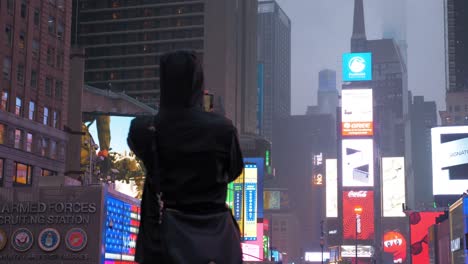 silhouette-taking-picture-with-smartphone-at-night-on-time-square,-with-all-the-screens-on-the-buildings,-New-York-City