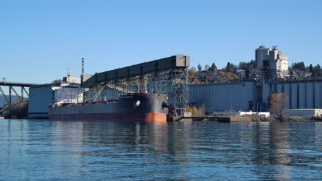 Cargo-ship-docked-at-industrial-port-with-grain-elevator-under-clear-blue-sky-in-Vancouver,-Canada