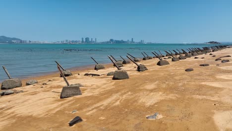 Drone-flight-over-golden-beach-in-Kinmen-Island,-金門,-Quemoy,-with-many-anti-landing-spikes-And-skyline-of-China-in-background---War-between-Taiwan-and-China