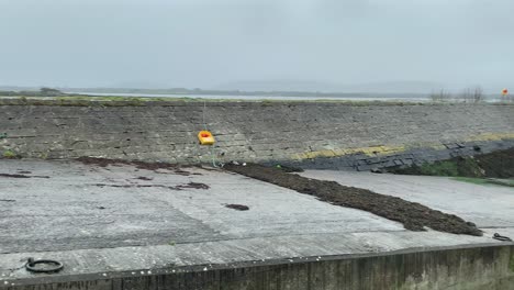 Pan-across-old-Tarrea-Pier-with-seaweed-and-over-turned-small-boat-on-cloudy-grey-day