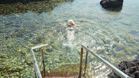 Hermosa-Mujer-Con-Sombrero-Nadando-En-El-Océano-Atlántico-En-Tenerife,-Vista-Posterior