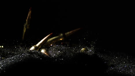 Slow-motion-shot-of-golden-6mm-ARC-bullets-falling-on-black-sand,close-up