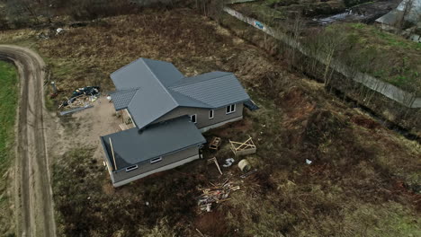New-house-with-gray-roof-and-dirt-driveway-road-in-muddy-field,-drone