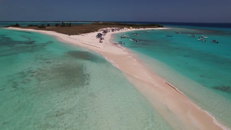Los-roques-archipelago-with-clear-turquoise-water,-boats,-and-sparse-crowds-on-a-sunny-day,-aerial-view