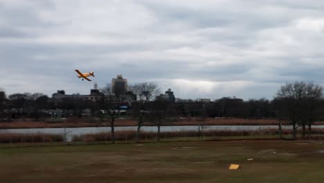 A-yellow-remote-control-airplane-flying-in-a-park-with-a-lake-on-a-cloudy-day