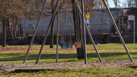 Empty-swings-in-park-with-passing-train-in-background,-sunny-day