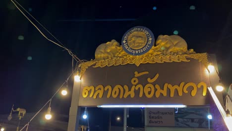 Vista-Nocturna-De-La-Puerta-De-Un-Templo-Tailandés-Adornada-Con-Esculturas-Doradas,-Iluminada-Por-Luces-Colgantes
