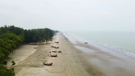 Aerial-of-a-beach-coastline-as-fisherman-get-their-boats-ready-on-a-foggy-morning-in-Kuakata,-Bangladesh