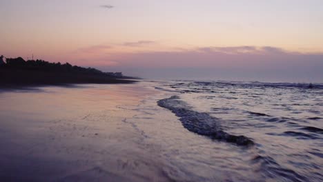 Atemberaubender,-Farbenfroher-Sonnenuntergangshimmel,-Der-Sich-Auf-Wasser-Und-Nassem-Sand-Spiegelt,-Während-Sanfte-Wellen-An-Einen-Strand-Rollen