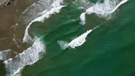 Top-view-of-beautiful-green-ocean-waves-crashing-onto-sandy-beach