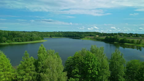 Aerial-drone-forward-moving-shot-over-a-lake-surrounded-by-lush-green-forest-on-a-bright-sunny-day
