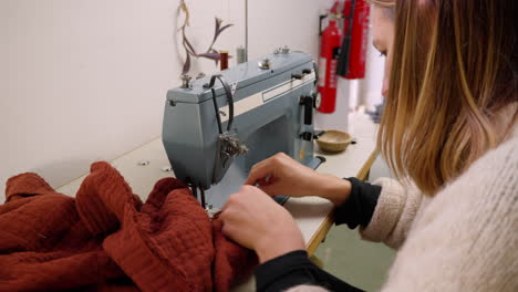 Wide-shot-of-caucasian-seamstress-sewing-red-fabric-with-a-sewing-machine