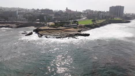 Waves-crashing-against-the-cove-in-La-Jolla,-California-on-an-overcast-day,-aerial-view-wide-shot