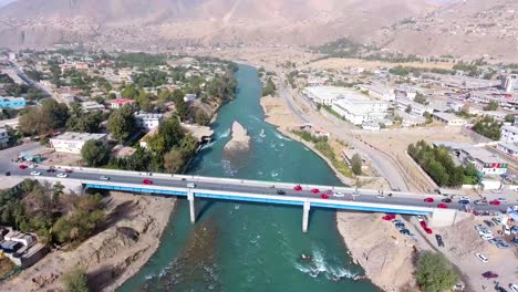An-aerial-shot-of-two-bridges-crossing-a-river-in-a-village,-with-cars-crossing-the-bridge