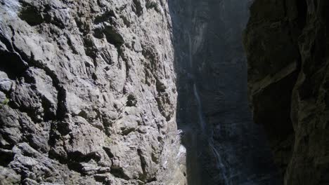 Sonnenlicht-Trifft-Auf-Felsen-Mit-Fließendem-Wasserfall-In-Der-Ferne-|-Grindelwald-Schweiz-Höhle-Im-Gletschercanyon,-Europa,-4k