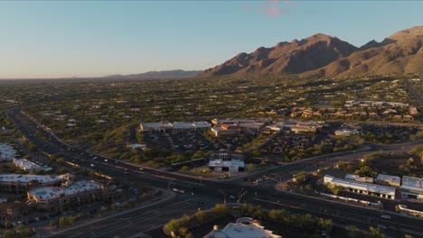 Drone-Shot-Hovering-Over-Busy-Tucson-Intersection,-Traffic-Moving-Quickly-at-Rush-Hour-in-Catalina-Foothills,-Mountains-in-Background-with-Cars-Below