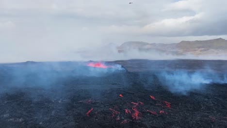 Helicopter-flies-above-Fagradalsfjall-volcano-as-smoke-and-steam-rise-across-barren-black-landscape