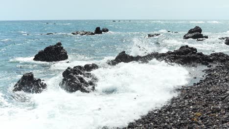 Ocean-waves-crash-on-jagged-rocky-boulders-sticking-out-of-water,-slow-motion