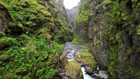 River-erodes-and-downcuts-rock-with-sheer-walls-of-mossy-vegetation,-aeriall-pullback