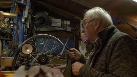 Pensive-senior-caucasian-mechanic-arranges-tools-in-a-a-dark-workshop
