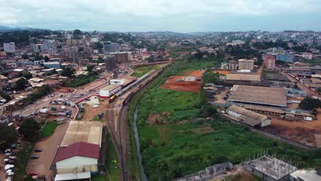 Aerial-view-rising-over-a-river,-following-the-city-railroad,-in-cloudy-Yaounde,-Cameroon