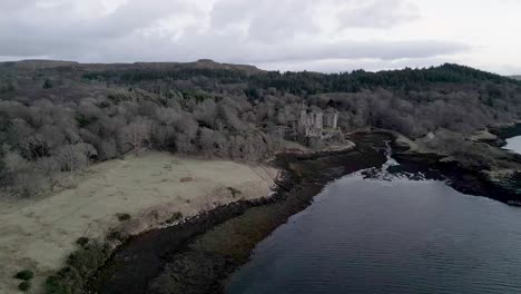 Dunvegan-castle-on-the-isle-of-skye,-surrounded-by-woodland-and-the-sea,-under-a-cloudy-sky,-aerial-view